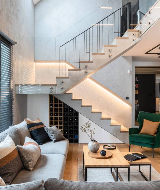 Stylish composition of stairs in living room interior. Grey sofa, green velvet armchair, coffee table and minimalist personal accessories. Modern home decor. Template.